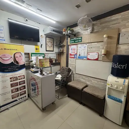 A tiled waiting area with a reception desk, a wall-mounted television, cushioned stools along the wall and a water dispenser in the corner.