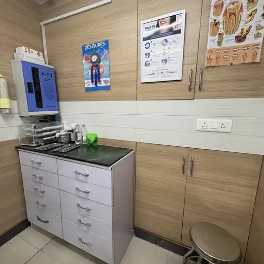 A wall-mounted sterilising cabinet above a drawer unit holding instrument trays, next to wooden cupboards and framed dental charts.