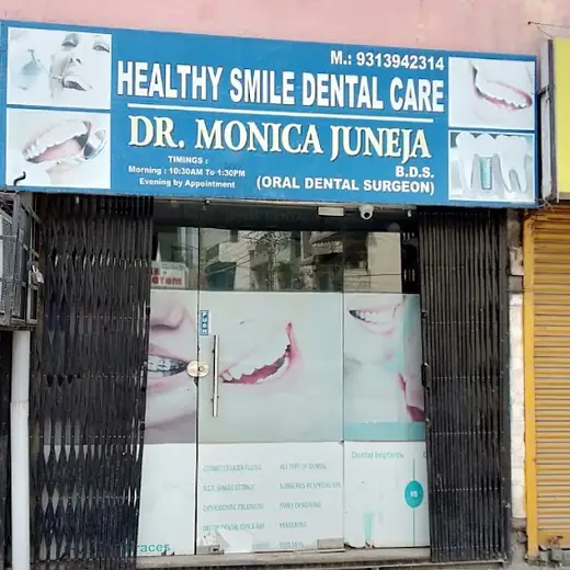 The clinic seen from the street in daylight: a blue signboard above a glass door set into the shuttered ground floor of a pink building.